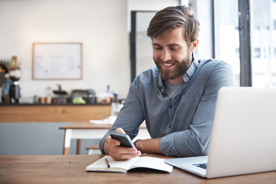 Jeune homme barbu regardant son smartphone en souriant